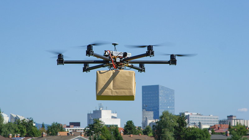 UAV drone delivery delivering big brown post package into urban city