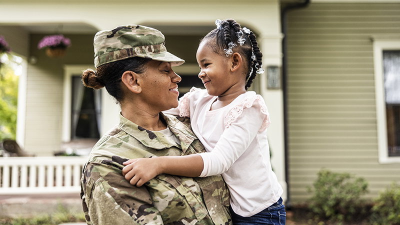 Portrait of female U.S. soldier in uniform with young daughter in front of home