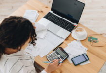 Report: Detroit is Least Expensive City in U.S. for Household Bills Woman working on her bills with a laptop and a calculator